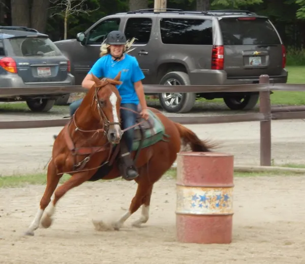 A rider in a helmet turns a sorrel horse around a barrel