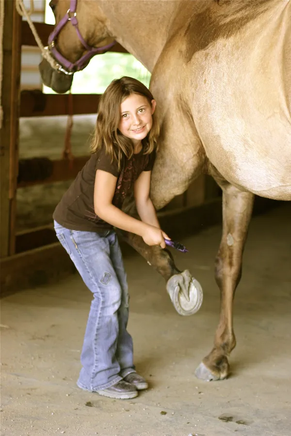 A girl smiles while cleaning a horse's hoof