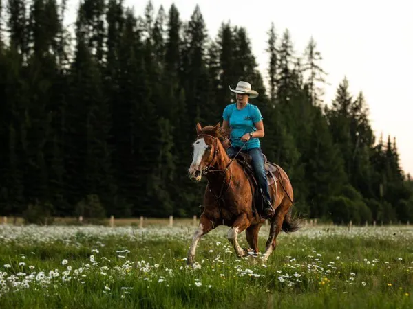 cowgirl loping a sorrel horse with a blaze through a field of wildflowers at dusk at Western Pleasure Guest Ranch