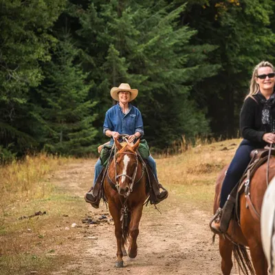 Woman in a cowboy hat riding a sorrel horse down the trail