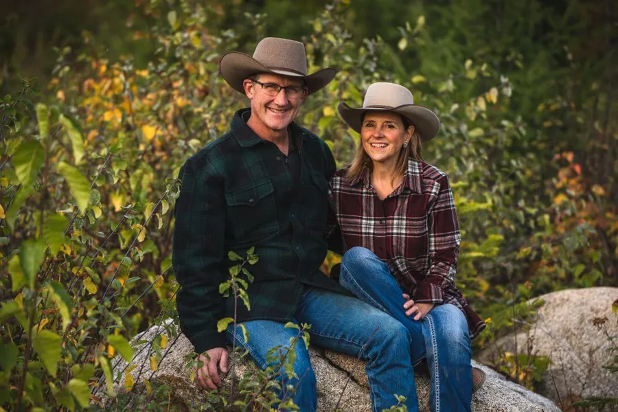 Roley and Janice Schoonover sit on a large rock with Fall foliage in the background