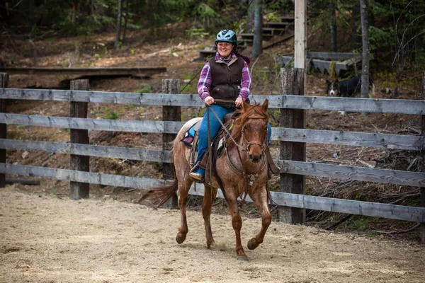 Woman trotting on a horse in an arena lesson at dude ranchsmiling