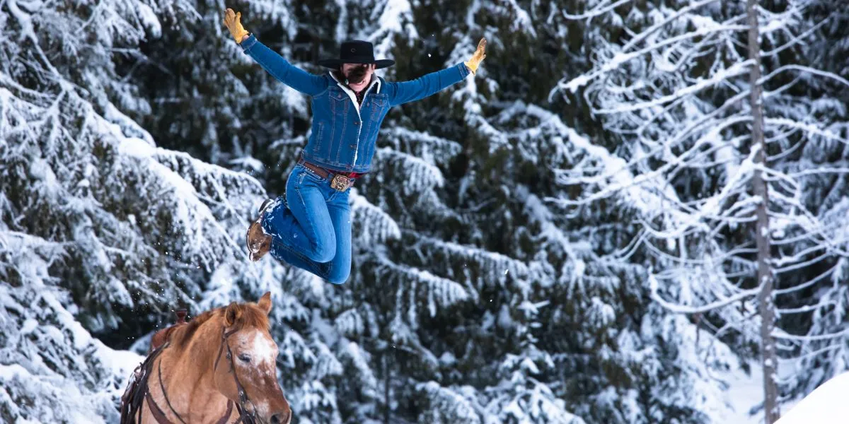 Cowgirl with her hands in the air jumping off horse into snow bank