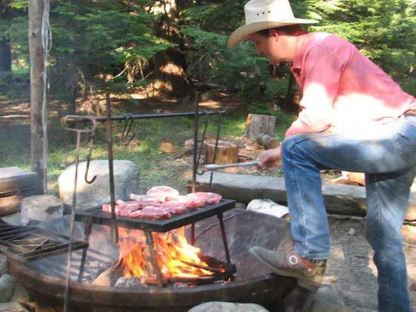 A cowboy grills steaks over an open fire on the dinner ride