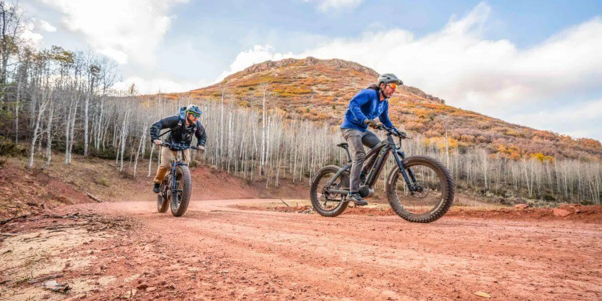 two men riding ebikes on a red dirt road