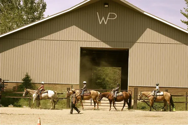 children riding horses in an arena with and indoor arena in the background