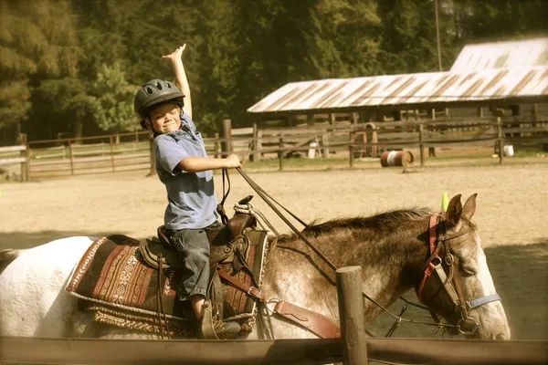 A young rider in a helmet raises an arm in celebration on horseback in the arena