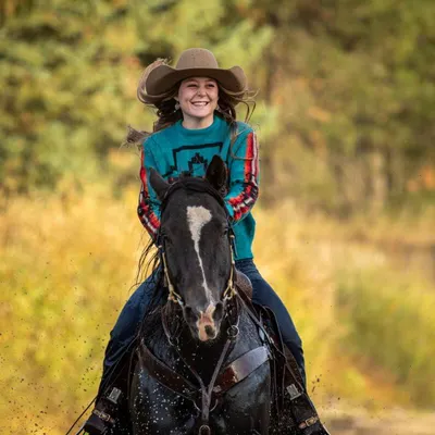 Blonde girl smiling and laughing while riding her horse through water