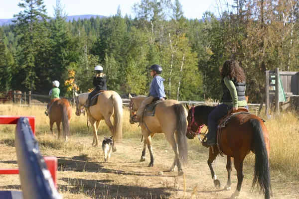 Young riders in helmets head out on a trail ride with a wrangler