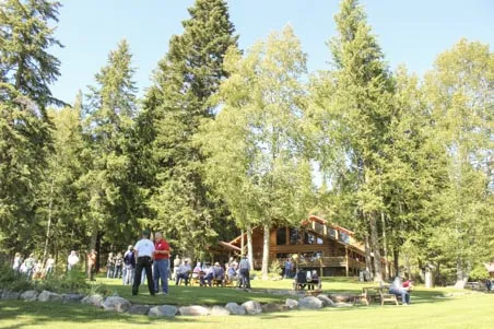 people standing on a green lawn in front of a log lodge