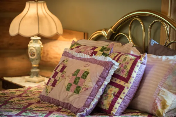 Brass bed with patchwork quilt pillows beside a lamp