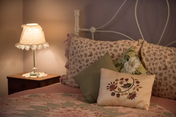 Bed with floral pillows and a lace-shaded lamp on the nightstand