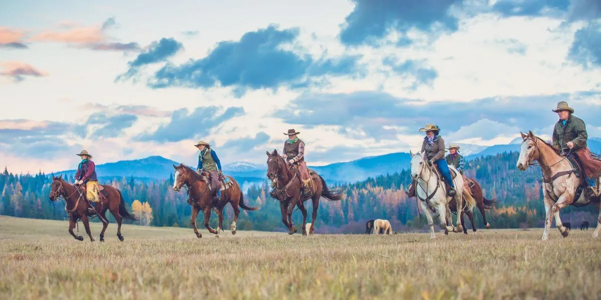 6 riders on horseback loping through a field with a dramatic cloudy sky overhead