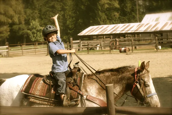 A young rider in a helmet raises an arm in celebration on horseback in the arena