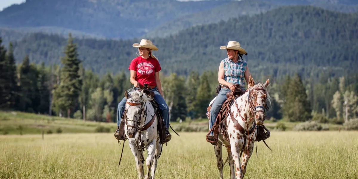 two women ride leopard Appaloosa horses across a green field