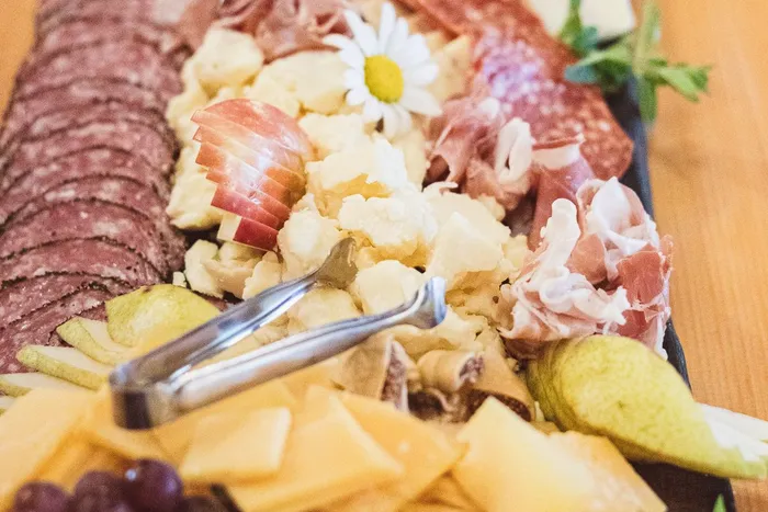 Close-up of a charcuterie board with salami, prosciutto, crumbled cheese, sliced apple and daisies