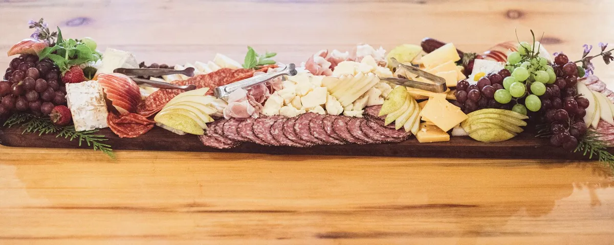 A long charcuterie board of salami, prosciutto, cheeses, grapes, apples and pears on a wooden table