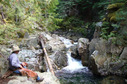 Cowboy sitting on rocks looking out at a small waterfall