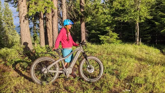 A woman stands next to an eBike while taking a rest on a mountain ride