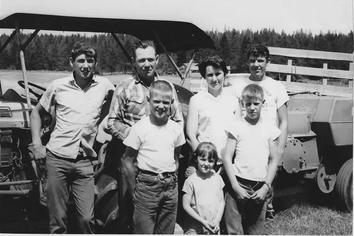 black and white photo of a family in jeans and white shirts standing in front of a tractor in a hay field
