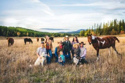 multi generational family photo with a family sitting in a field with two dogs and a horse next to them
