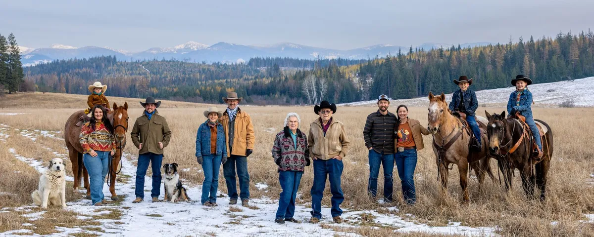 The family standing in a snowy hayfield below the mountains, with two dogs, and three children on horseback