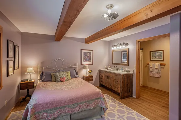 White iron bed with a pink quilt in Grandma's Room, beside a wood vanity and the door to the bath