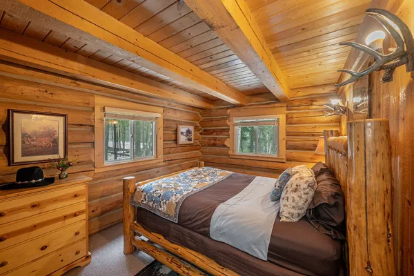 Log bed with a patchwork quilt in the Hunter Cabin bedroom, with log walls and an antler light