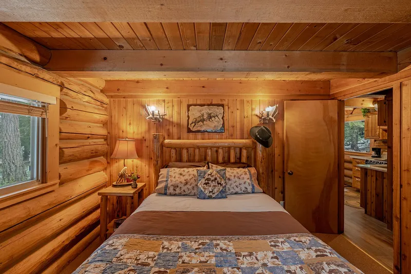 Main-floor bedroom of the Hunter Cabin, with a log bed, antler wall lights and the kitchen through the doorway