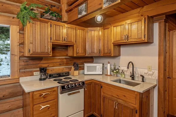 Hunter Cabin kitchen, with antler-handled wood cabinets, a stove and microwave, below the loft railing