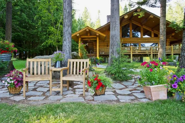Log lodge with large front windows, potted flowers and two chairs in the foreground
