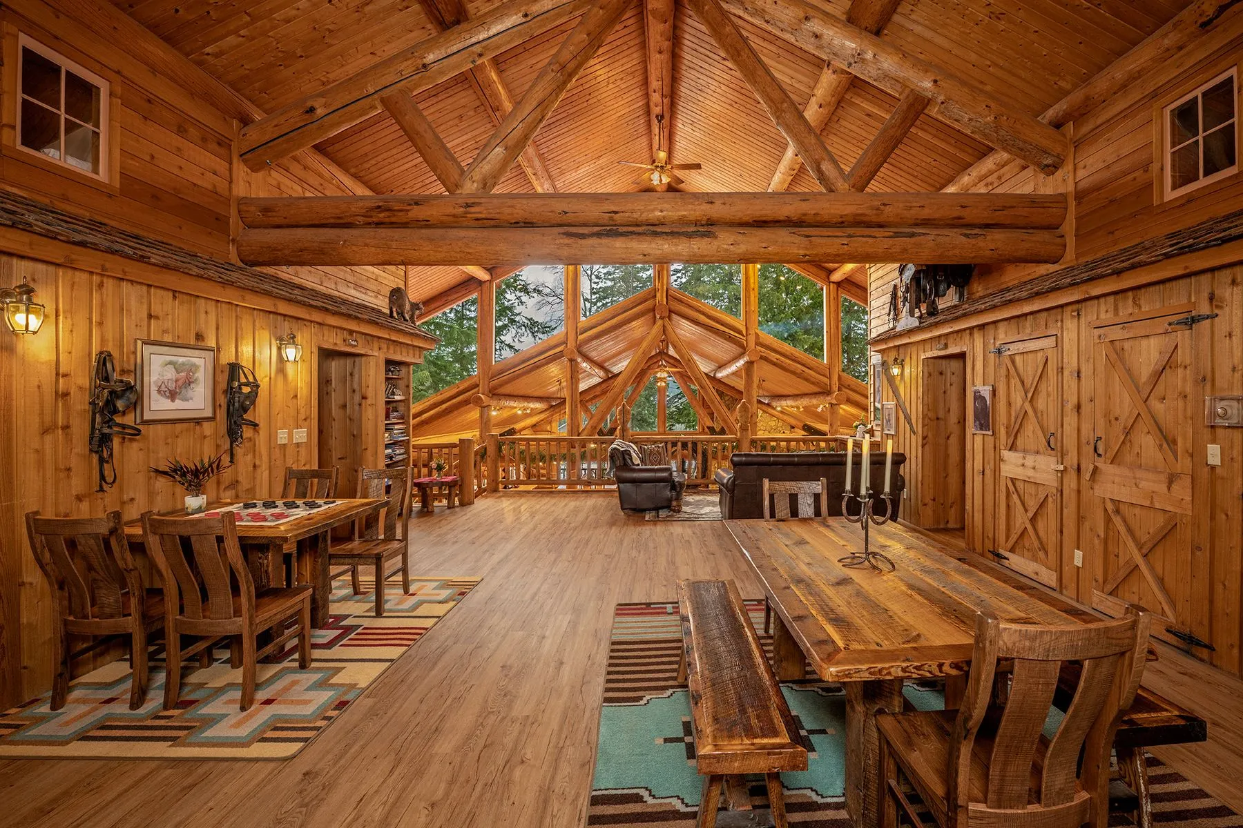 Lodge loft with log trusses, dining tables on Southwestern rugs, and leather couches by the log railing