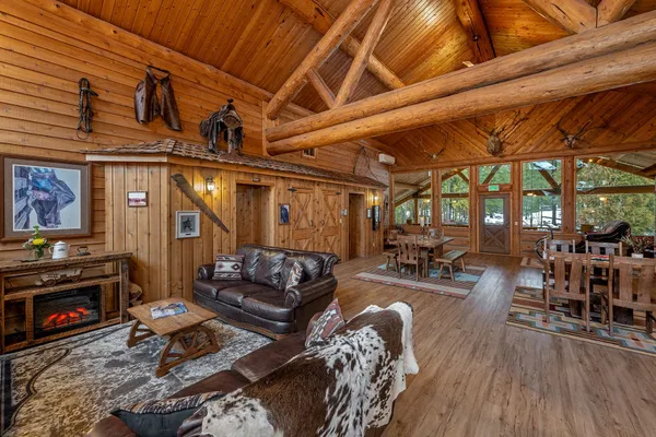 Lodge loft sitting area with leather couches, a cowhide throw, a wagon-wheel coffee table and an electric fireplace, with tables by the windows