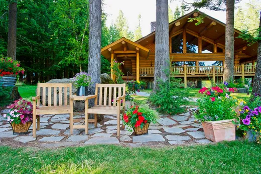 Large log lodge in the background with relaxing chairs in the foreground with flowers around them