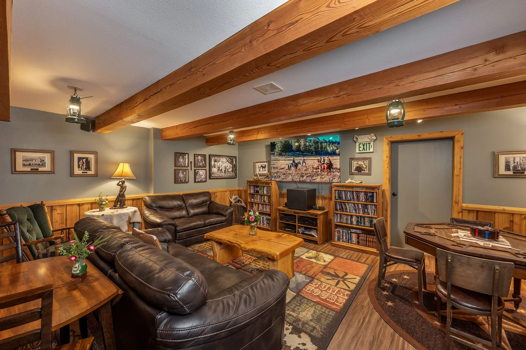 Lodge rec room with leather couches, a log coffee table, shelves of movies, a TV and a card table