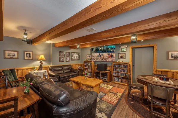 Lodge rec room with leather couches, a log coffee table, shelves of movies, a TV and a card table