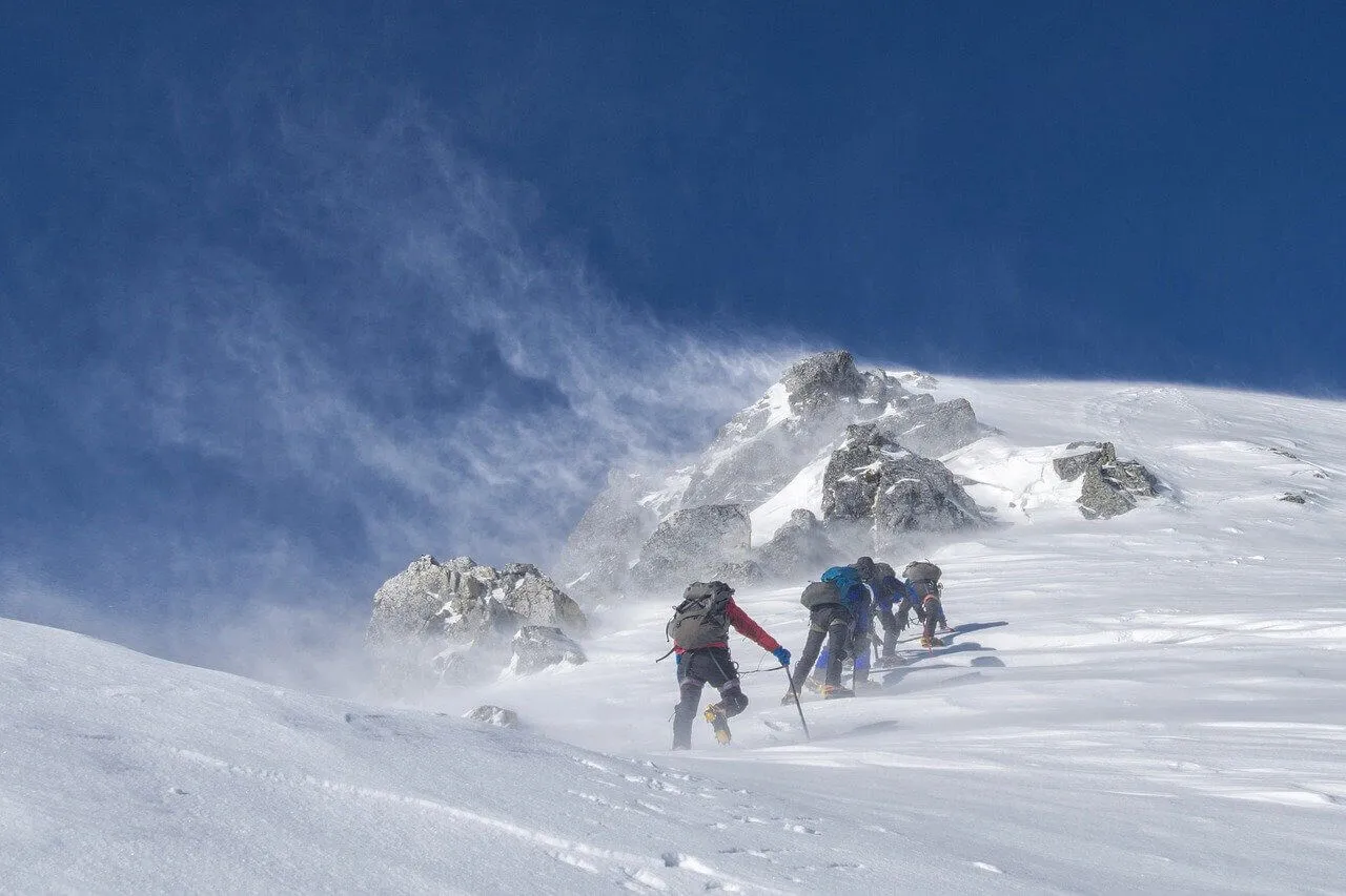 Adventure travel of four men climbing a wind-blown snow-covered mountain summit.
