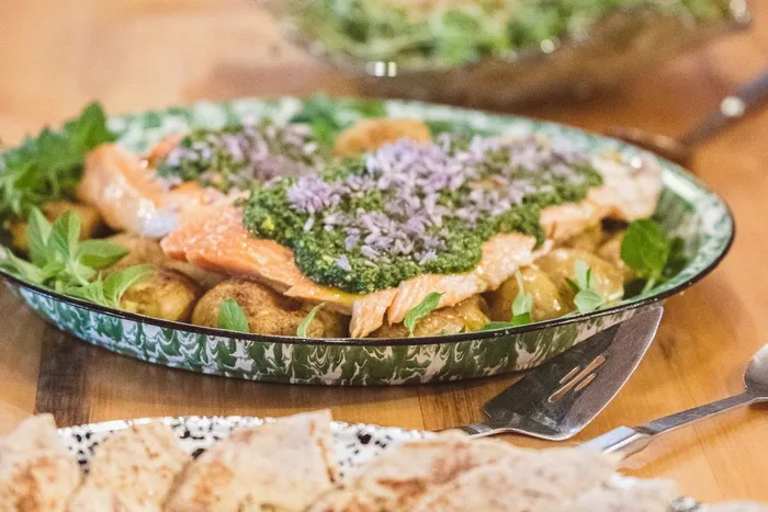 Salmon with green herb sauce on potatoes, beet hummus with flatbread, and salads on a wooden table