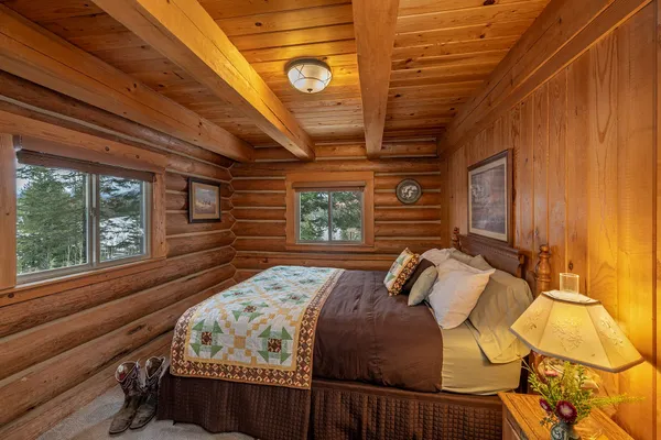 Main-floor bedroom of the Settler Cabin, with a quilted bed, log walls and cowboy boots on the floor