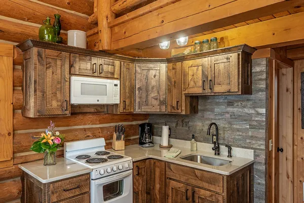 Settler Cabin kitchen, with rustic wood cabinets, a stove, microwave and coffee maker, below the loft railing