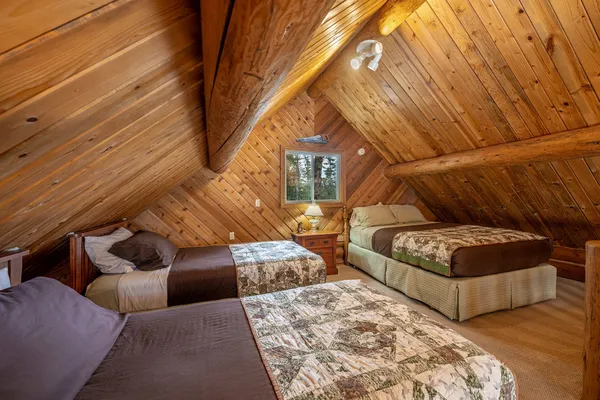 Open loft of the Settler Cabin, with quilted beds under the sloped wood ceiling