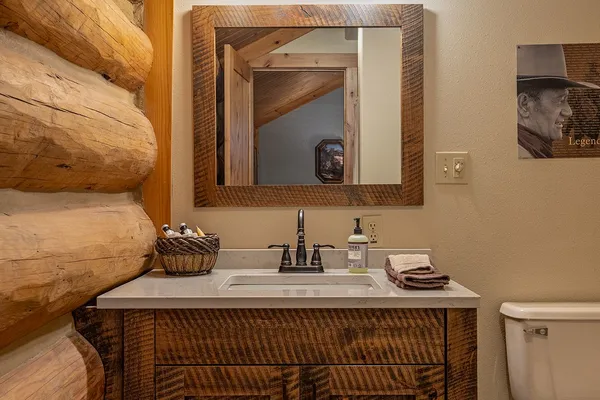 Rustic wood vanity and mirror in the Duke room's bathroom, with a cowboy portrait on the wall