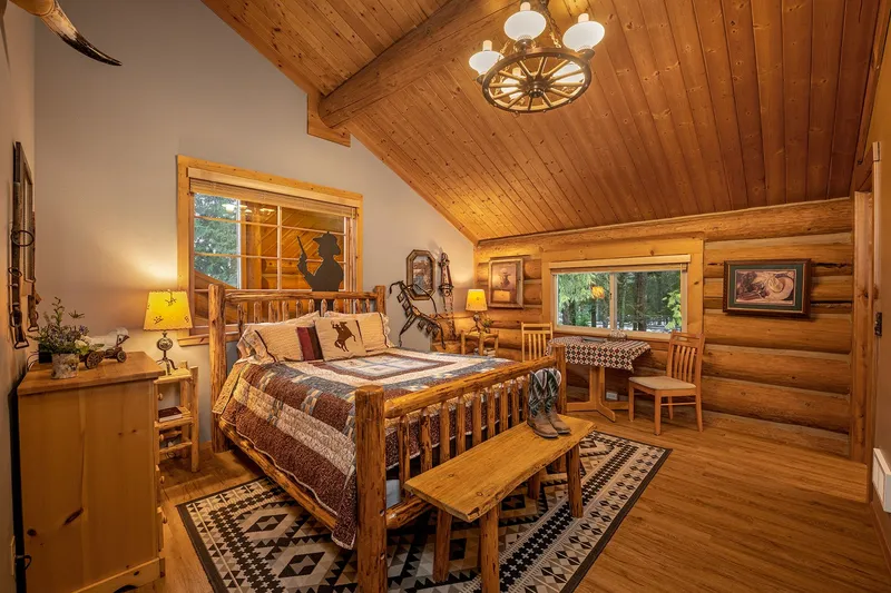 Log bed with a patchwork quilt in the Duke room, under a wagon-wheel chandelier and a sloped wood ceiling