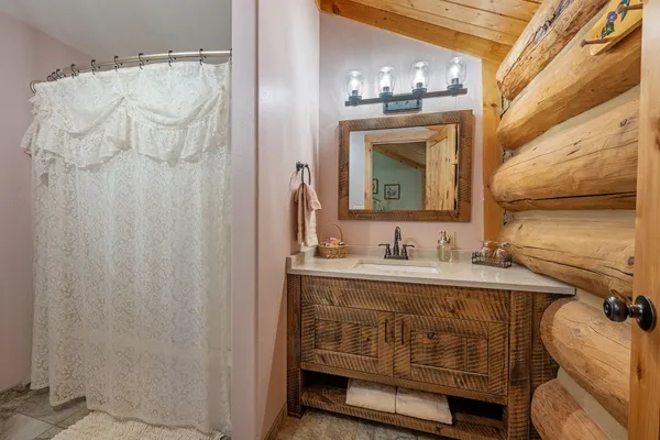 The Miss Belle room's bathroom, with a rustic wood vanity, a lace shower curtain and a log wall