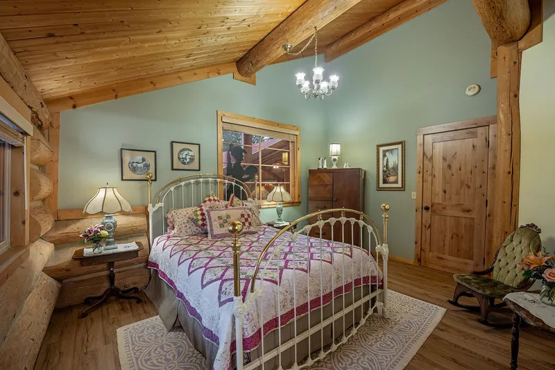 Brass and white iron bed with a pink and purple quilt in the Miss Belle room, with sage green walls and a small chandelier