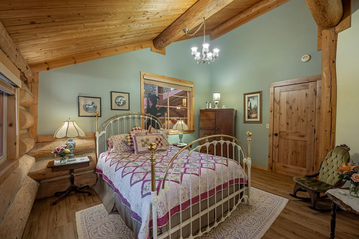 Brass and white iron bed with a pink and purple quilt in the Miss Belle room, with sage green walls and a small chandelier