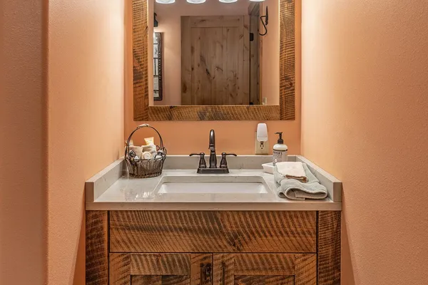 Rustic wood vanity and mirror in the Nez Perce room's bathroom, under a light fixture with tipis and a rider