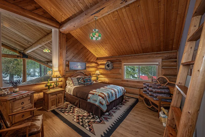The Siesta room, with a bed in a Southwestern blanket, a carved wood bench and a ladder to the loft