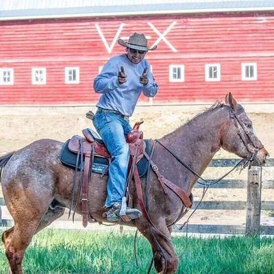 Cowboy smiling for camera while riding his horse past a big red barn at Western Pleasure Guest Ranch