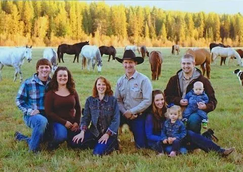 A family sits together in a meadow with horses grazing behind them